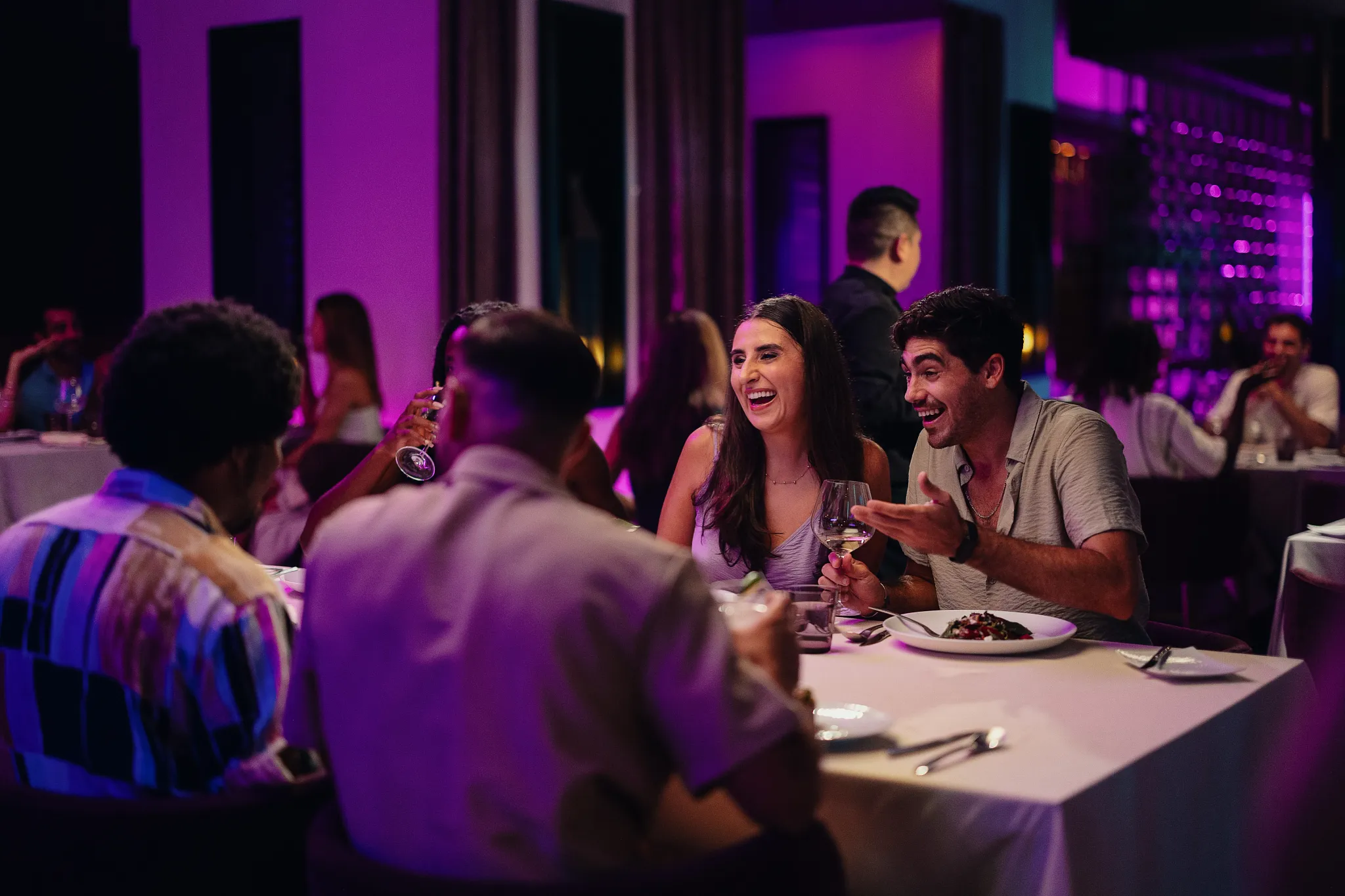 Friends enjoying a lively dinner with wine in a modern, purple-lit dining venue at Breathless Riviera Cancun.