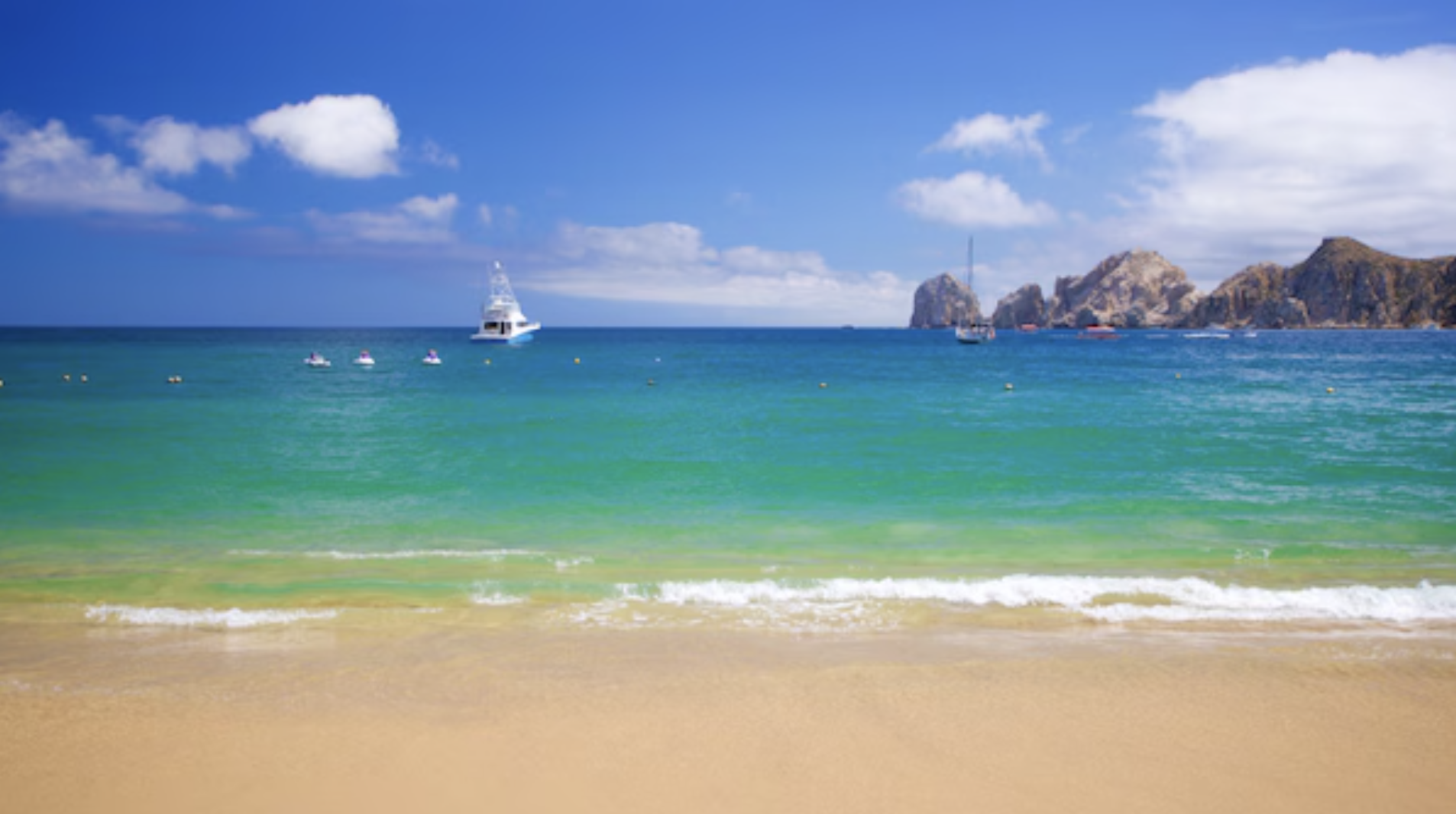 Scenic view of Cabo San Lucas Bay with turquoise water, golden sand, and Land’s End rock formations in the distance.